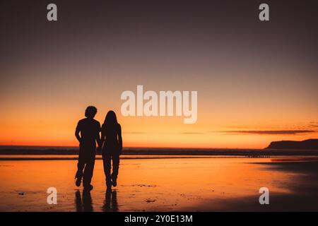 La silhouette di una coppia che cammina sulla spiaggia dopo il tramonto Foto Stock