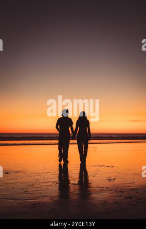 La silhouette di una coppia che cammina sulla spiaggia dopo il tramonto Foto Stock