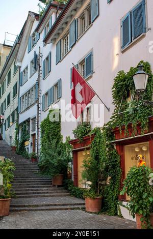 28-08-2024 Zurigo, Svizzera. Piccoli negozi su una strada stretta con scale in pietra che conducono al famoso punto panoramico di Lindenhof. Soleggiato giorno d'estate, niente fastidio Foto Stock