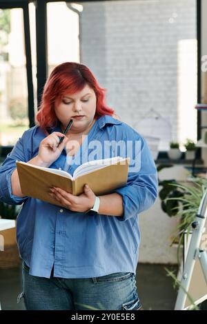 Una donna di grandi dimensioni con i capelli rossi legge attentamente un libro in uno spazio luminoso e arioso. Foto Stock