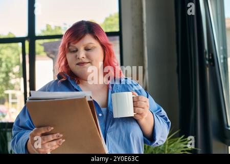 Una donna di grandi dimensioni con capelli rosa vivaci legge documenti importanti, una tazza bianca nell'altra mano. Foto Stock