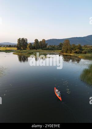 Coppia che pagaiano su una canoa rossa vicino alle ninfee gialle nel lago calmo, direttamente sopra il tiro. Natura selvaggia e bellezza della natura. Foto Stock