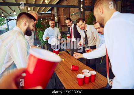 I colleghi fanno una pausa divertente dal lavoro con una sfida di birra pong, godendosi un momento di relax alla birra locale, bevendo birra Foto Stock