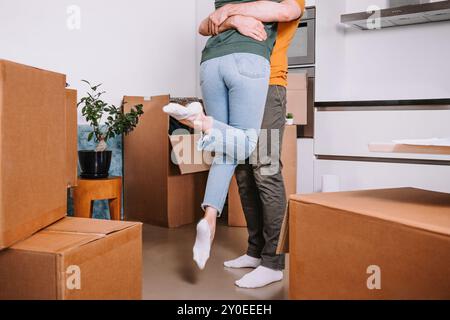 La famiglia si solleva e gira con gioia tra le scatole in movimento, celebrando il loro trasferimento in una nuova casa, in posa felice Foto Stock