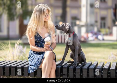 Una giovane donna siede in un parco cittadino con il suo cane, un Weimaraner. Foto Stock