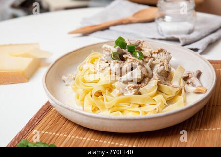 Un delizioso piatto di tagliatelle cremose condite con funghi chanterelle e cipolle verdi, servite con formaggio sul tavolo Foto Stock