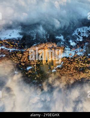 Vista aerea che cattura sentieri tortuosi attraverso paesaggi innevati e ricoperti di nebbia. Il contrasto tra terreno innevato e nuvole avvolgenti crea una scena drammatica ed eterea, mettendo in risalto la bellezza della natura. Foto Stock