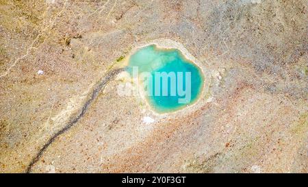 Un piccolo tarn alpino annidato nel terreno roccioso dell'Austria mostra vibranti acque turchesi sotto il cielo limpido, circondato da bellezze naturali e serena natura selvaggia, invitante tranquillità ed esplorazione. Foto Stock