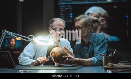 Due archeologi prendono misure di cranio umano antico, studiano resti fossili, usano un computer tablet. Scienziati o storici conducono ricerche scientifiche in laboratori archeologici avanzati di notte. Foto Stock