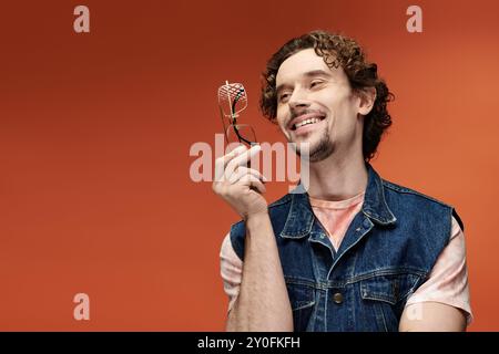 Un uomo affascinante gode di un momento, sorridendo e tenendo gli occhiali su uno sfondo luminoso. Foto Stock