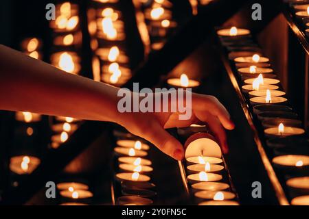 La mano di una donna che accende una candela in una chiesa Foto Stock