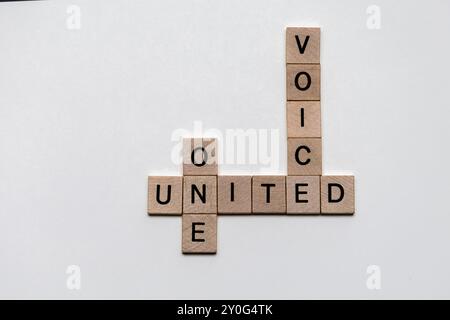 Primo piano di piastrelle di legno che formano un puzzle di parole incrociate con le parole "uno", "voce" e "Unito": Concetto di unità e azione collettiva Foto Stock