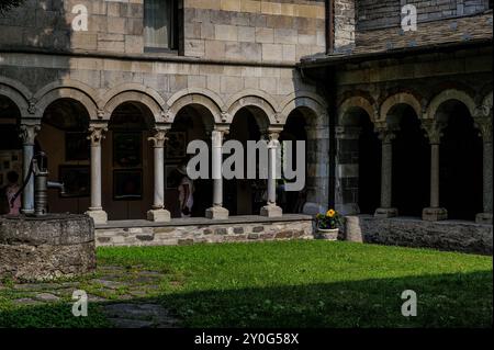 Nella passeggiata del chiostro presso l'Abbazia di Piona, Colico, Lombardia, Italia, i visitatori possono ammirare le opere d'arte in mostra. Sulla sinistra si trova una testa di pozzo sormontata da una pompa manuale. Il chiostro fu costruito intorno al 1242. Foto Stock