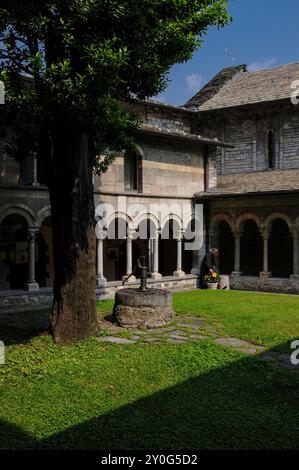 Angolo del chiostro, costruito intorno al 1242, presso l'Abbazia di Piona, Colico, Lombardia, Italia. Il chiostro è annesso alla chiesa abbaziale della Chiesa di San Nicola (a destra), che risale alla fine del 1000 o all'inizio del 1100 Davanti al chiostro si trova una testa di pozzo sormontata da una pompa manuale. Foto Stock