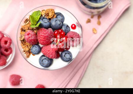 Gustoso yogurt con frutti di bosco freschi, muesli e menta in vetro sul tavolo grigio, vista dall'alto Foto Stock