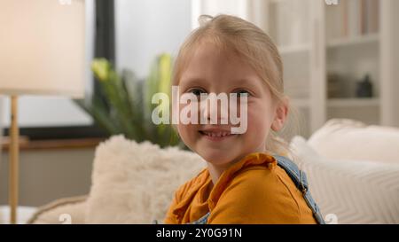 Positivo felice Caucasico bambino scolaresca gen z bambino posa guardando la macchina fotografica da sola a casa sano ampio toothy sorriso carino viso allegro bionda piccolo Foto Stock