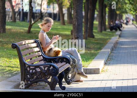 Ragazza che usa lo smartphone seduto su una panchina con il suo cane nel parco cittadino Foto Stock