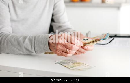 Le mani di una donna anziana che tallona banconote e monete in Euro in cucina Foto Stock