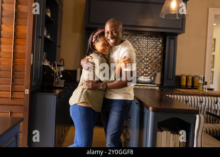 Una coppia multirazziale sorridente che si abbraccia in cucina e si diverte a casa Foto Stock