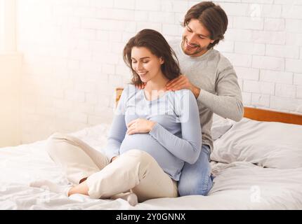 Amorevole marito rendendo massaggio alla schiena per il suo felice moglie incinta Foto Stock