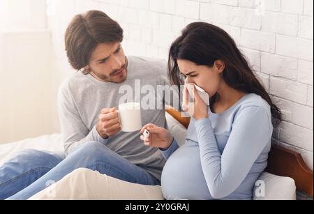 Il marito guardando dopo i suoi malati moglie incinta che soffrono di influenza Foto Stock