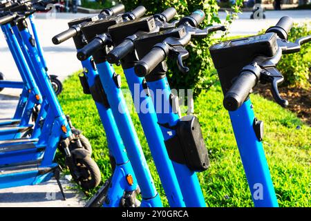 Gli scooter elettrici blu noleggiati parcheggiati nel parcheggio sono pronti per l'uso - questo è un veicolo molto familiare che ti consente di muoverti senza pol Foto Stock