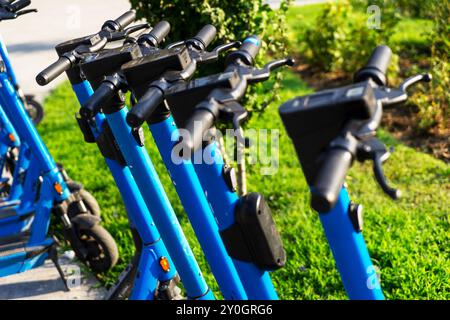 Gli scooter elettrici blu noleggiati parcheggiati nel parcheggio sono pronti per l'uso - questo è un veicolo molto familiare che ti consente di muoverti senza pol Foto Stock