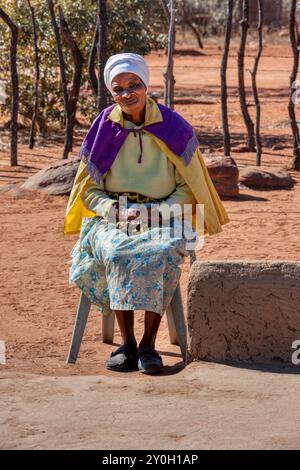 Anziana donna africana del villaggio seduta su una sedia nel cortile di sabbia Foto Stock