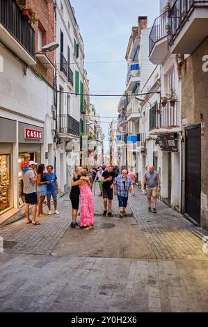 Sitges, Barcellona - 01 settembre 2024: Una vivace strada nel centro storico di Sitges con turisti che passeggiano sotto un cielo limpido riflette il fascino di Foto Stock