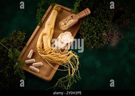 Radice di ginseng e supplementi su un vassoio di legno con sfondo verde fogliame. Foto Stock