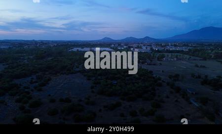 Paesaggio urbano che accende le luci al tramonto con le montagne sullo sfondo Foto Stock