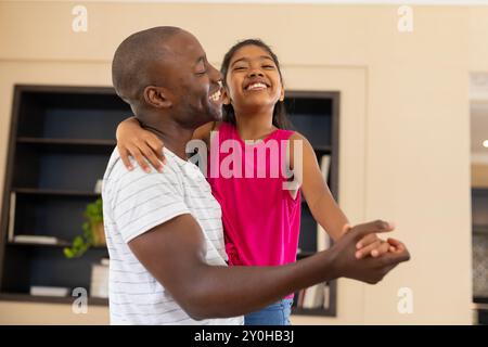 Padre e figlia ballano insieme, sorridono e si divertono con la famiglia a casa Foto Stock