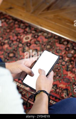 Tenere lo smartphone, la persona che naviga su uno schermo vuoto su un tappeto a motivi, copiare spazio Foto Stock