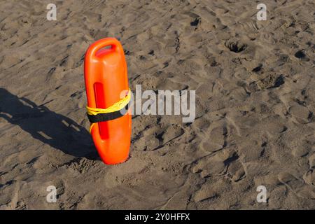 Una boa arancione del bagnino è saldamente piantata sulla spiaggia sabbiosa, indicando le misure di sicurezza in vigore per i nuotatori. Il colore brillante si distingue contro la sabbia abbronzata. Foto Stock