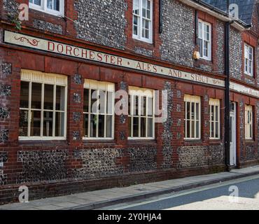 Edificio storico con facciata in pietra e mattoni che pubblicizza "Dorchester Ales and Stout" a Winchester, Regno Unito, in una giornata di sole Foto Stock