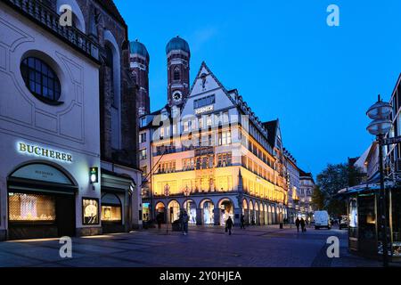 Monaco di Baviera, Germania - 18 aprile 2024: Vista esterna di Hirmer, la più grande casa di moda maschile. Le torri della Frauenkirche Foto Stock