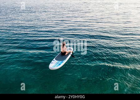 Donna pagaia in acque calme durante una giornata di sole in spiaggia. Foto Stock