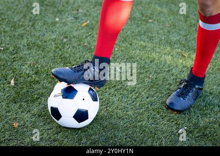 Calciare la palla da calcio su un campo di erba, giocare con calzini rossi e scarpe nere Foto Stock