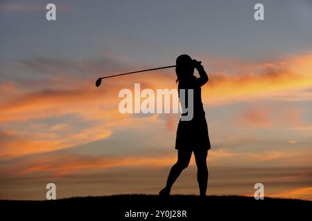 La silhouette di una donna golfista al tramonto che fa oscillare il golf club Foto Stock