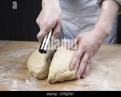 Una foto ravvicinata delle mani di una donna che usa un taglierino per tagliare una grande palla di impasto Foto Stock