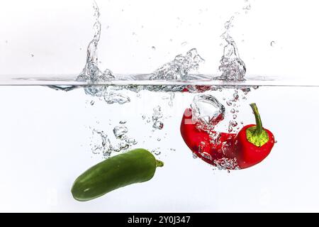 Un'immagine concettuale di un peperone rosso e un peperone verde caduti in acqua Foto Stock