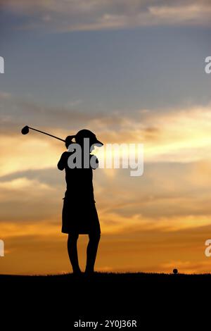 Una giovane ragazza in silhouette al tramonto fa oscillare il golf club al pallone Foto Stock