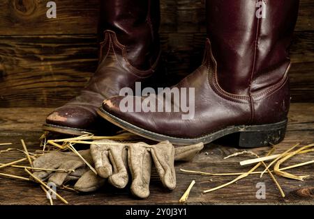 Un'immagine concettuale di stivali e guanti da cowboy indossati Foto Stock