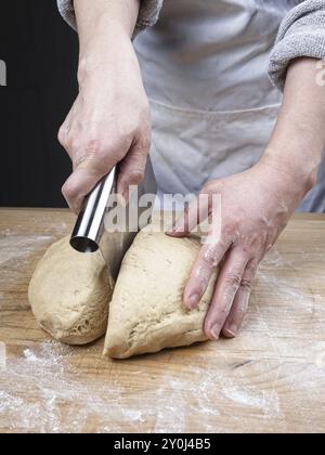 Una foto ravvicinata delle mani di una donna che usa un taglierino per tagliare una grande palla di impasto Foto Stock