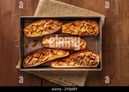 Melanzane arrosto con aglio, girato dalla parte superiore al buio su un rustico sfondo di legno con spazio di copia Foto Stock