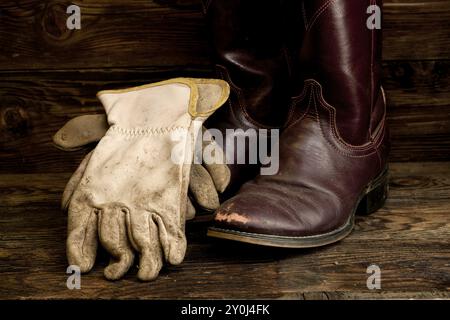 Un'immagine concettuale di stivali e guanti da cowboy indossati Foto Stock