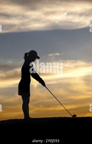 La silhouette di una donna golfista al tramonto che si allea sulla palla Foto Stock