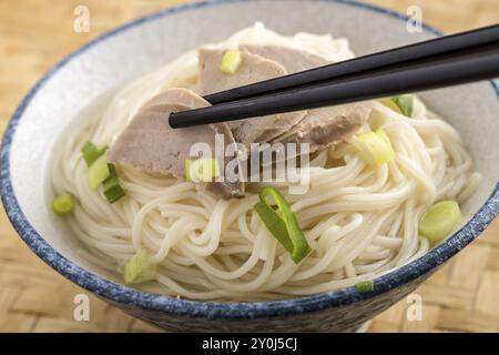 Una foto in studio dei bastoncini che afferrano una fetta di maiale sopra una ciotola di spaghetti Foto Stock