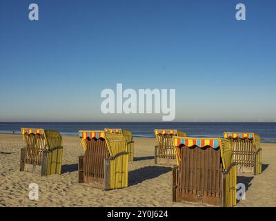 Diverse sedie a sdraio si trovano sulla spiaggia sabbiosa che si affaccia sul mare calmo in una giornata limpida e soleggiata, egmond aan zee, paesi bassi Foto Stock