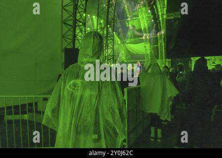 Persona in poncho verde per la pioggia durante un concerto serale con illuminazione verde del palcoscenico, Klostersommer, Calw Hirsau, Foresta Nera, Germania, Europa Foto Stock